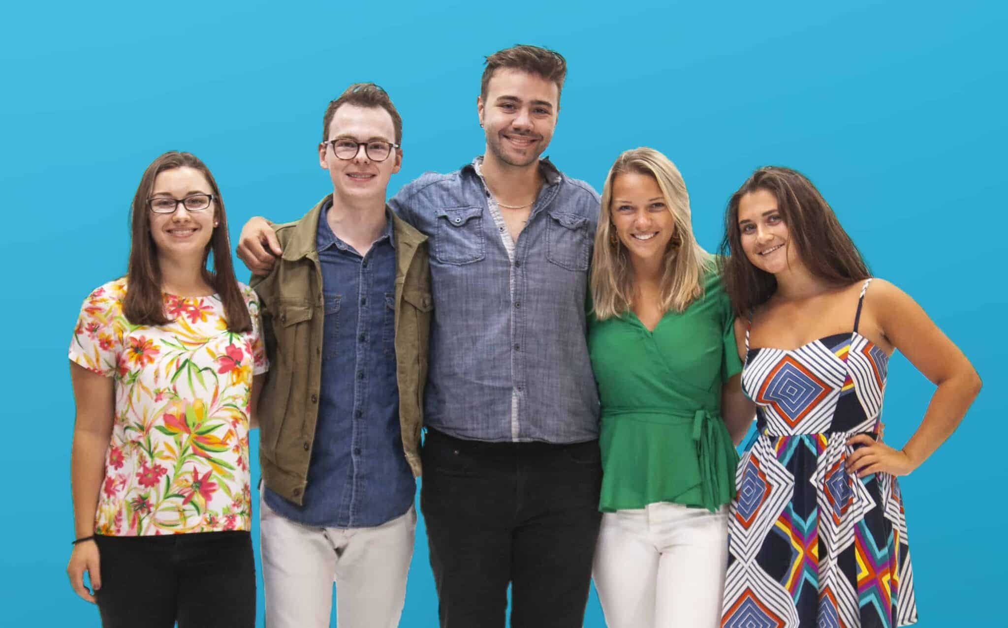Five smiling young professionals posing against bright blue background in colorful casual outfits