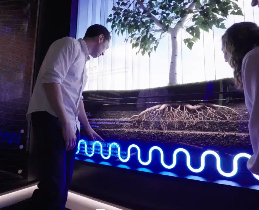 visitors interacts with an educational wall display featuring glowing plant roots and soil