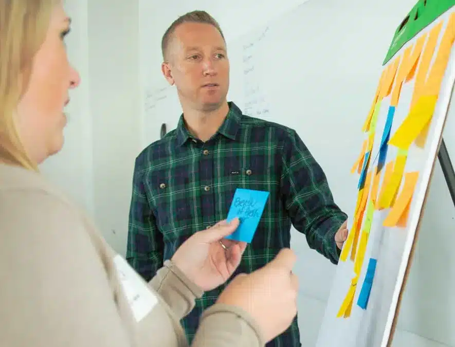 Facilitator in plaid shirt leads a brainstorming session with sticky notes on a whiteboard