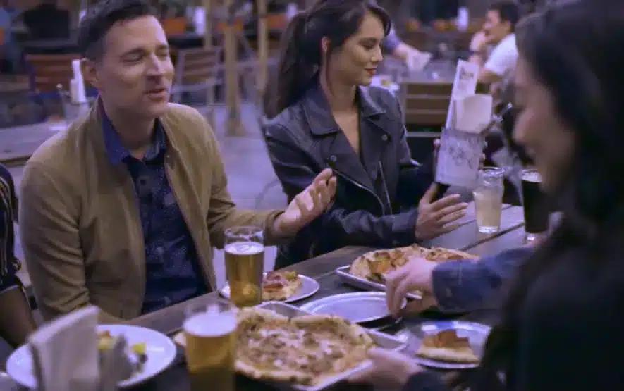 Friends enjoying outdoor dining with gourmet pizza, craft beer, and a lively atmosphere