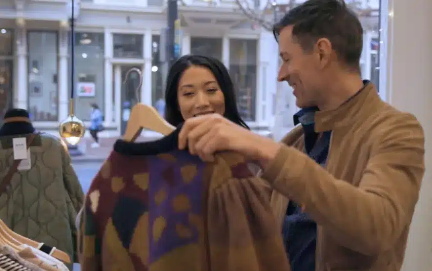 Couple shopping in a boutique, admiring a patterned sweater inside a stylish urban store