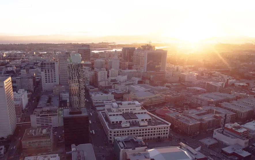 Aerial city view at sunset, with golden sunlight illuminating the skyline and urban streets