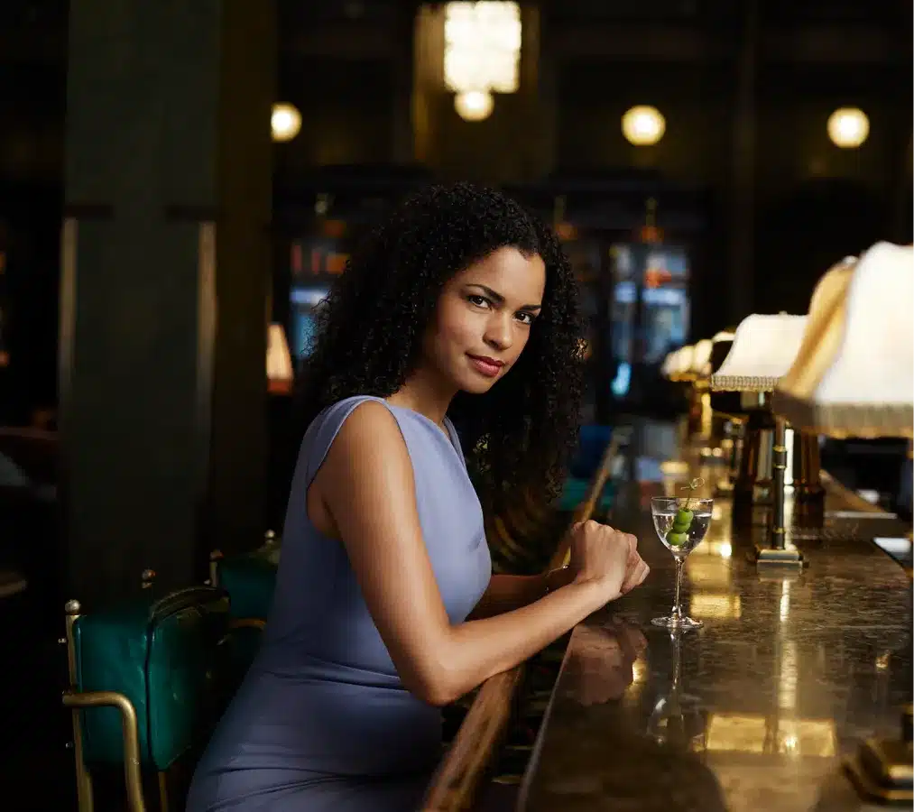 Elegant woman in a blue dress enjoying a cocktail at a dimly lit upscale bar