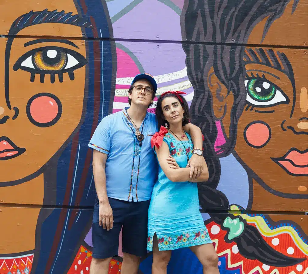 Two artists in vibrant blue outfits posing against an intricate urban street art mural