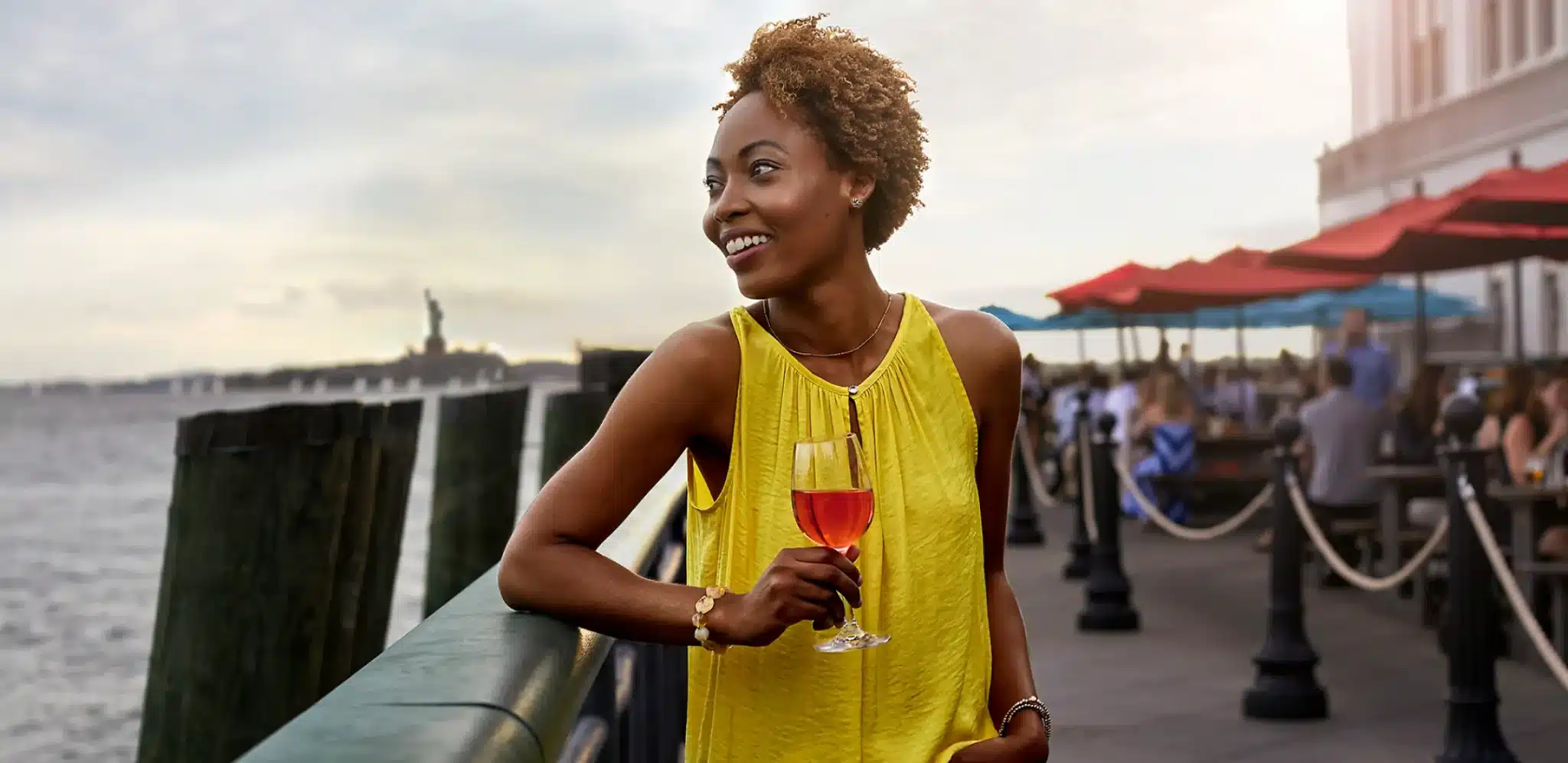 Smiling woman in a yellow dress enjoying a glass of rosé near the waterfront
