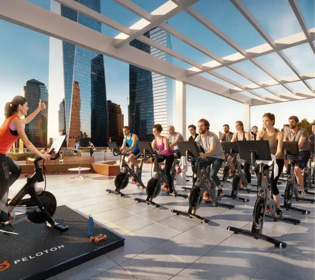 Group fitness class using Peloton bikes on an open-air rooftop with city skyscrapers behind them