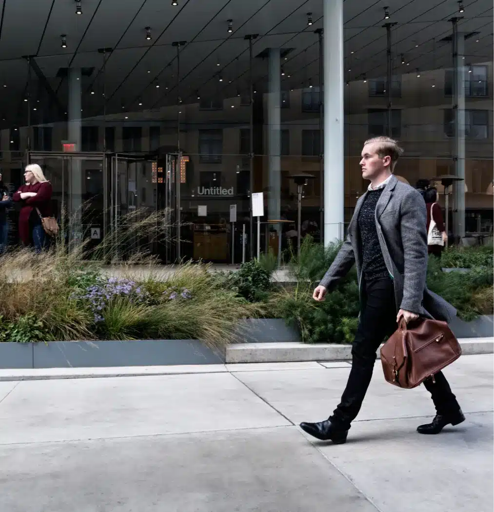 Urban professional carrying a leather bag, striding confidently past a contemporary business entrance