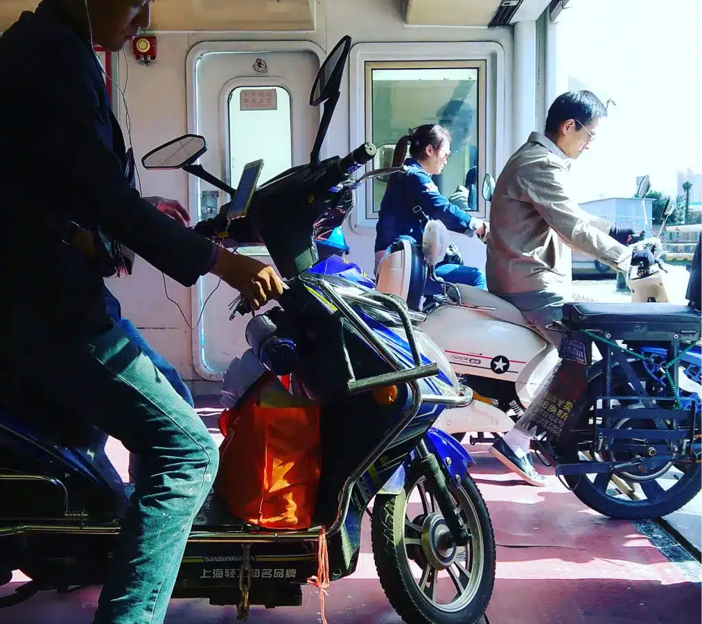 Local commuters riding scooters inside a ferry with bright sunlight streaming in