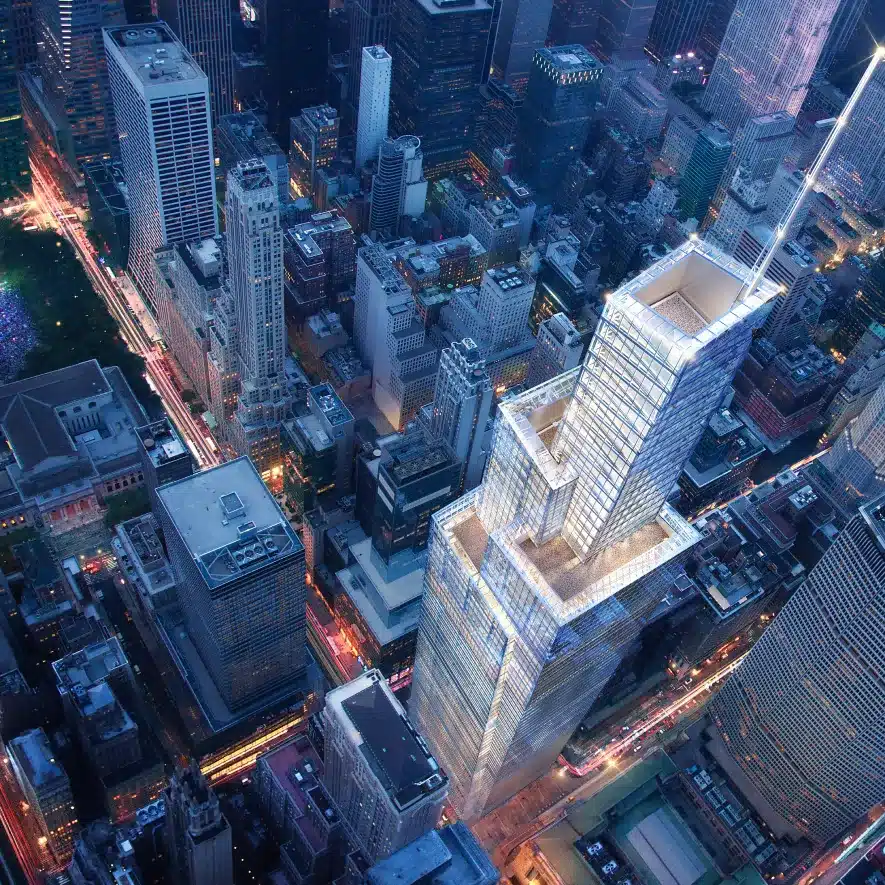 Aerial night view of a brightly lit glass skyscraper towering over the vibrant New York City streets