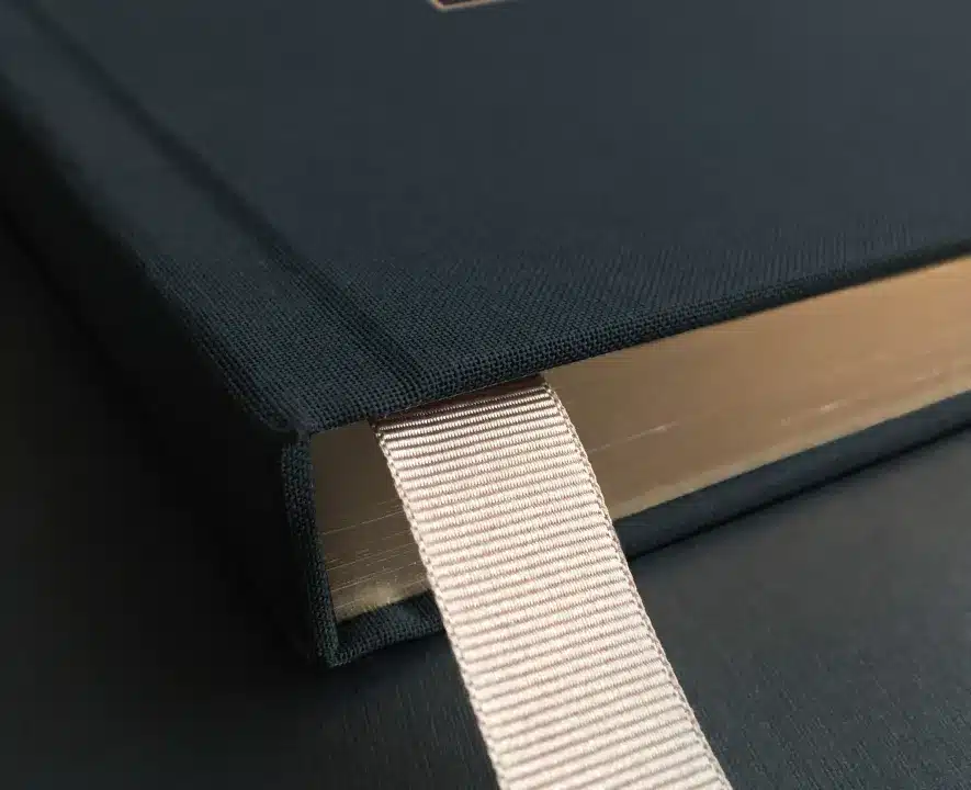 Close up of a luxurious hardcover book with gold-edged pages and a soft ribbon bookmark