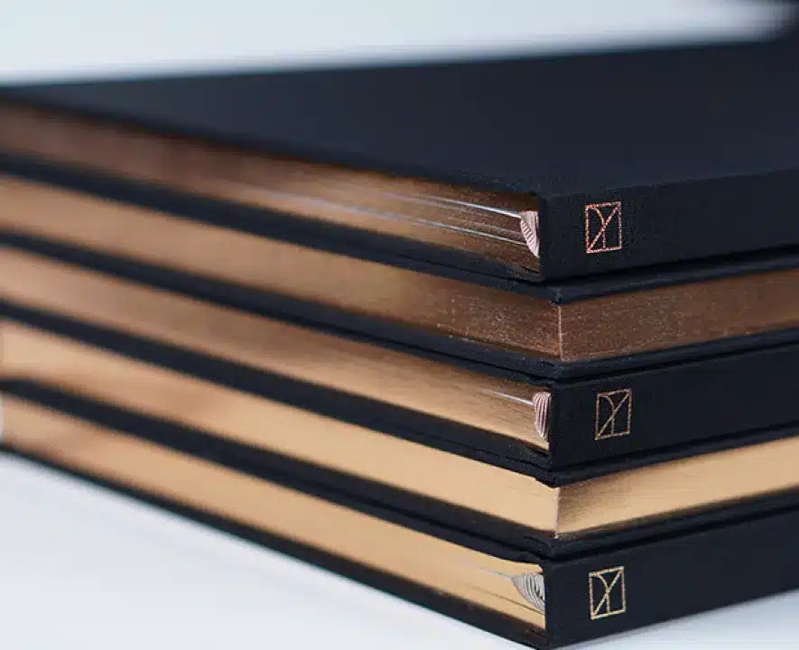 Stack of premium hardcover books with gold-accented edges and minimalist embossed logos