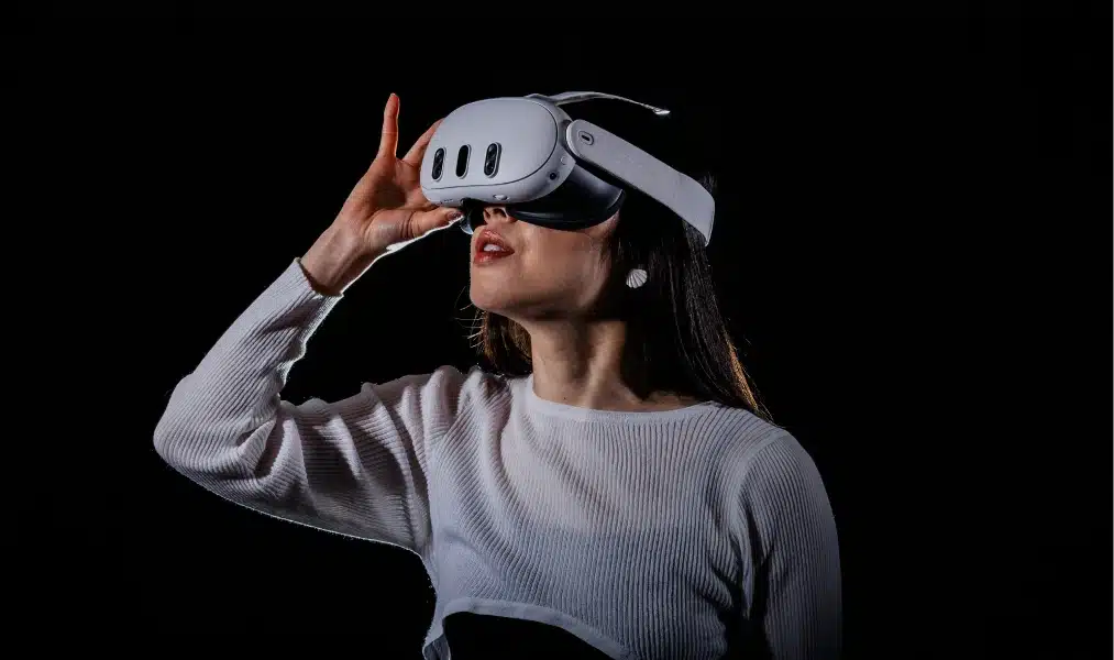Woman wearing white sweater using virtual reality headset in dark immersive environment
