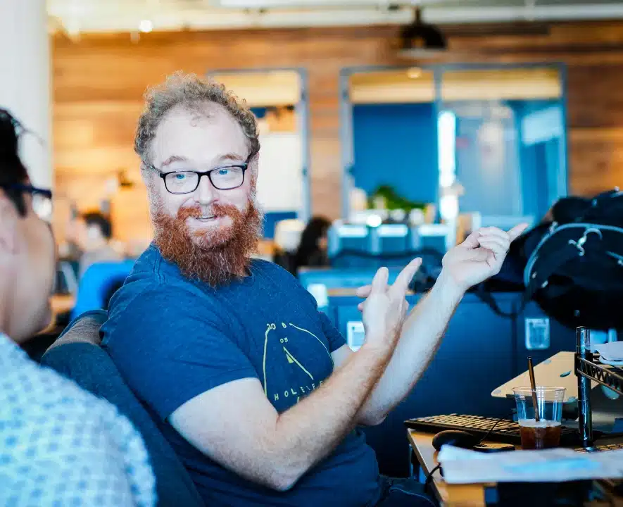 Bearded man with glasses smiling and gesturing during lively office conversation
