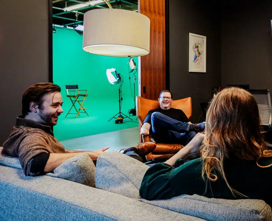 Three colleagues sitting and chatting casually near video production studio with green screen