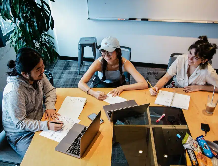 Group of interns brainstorming around a conference table with notebooks, laptops, and snacks nearby