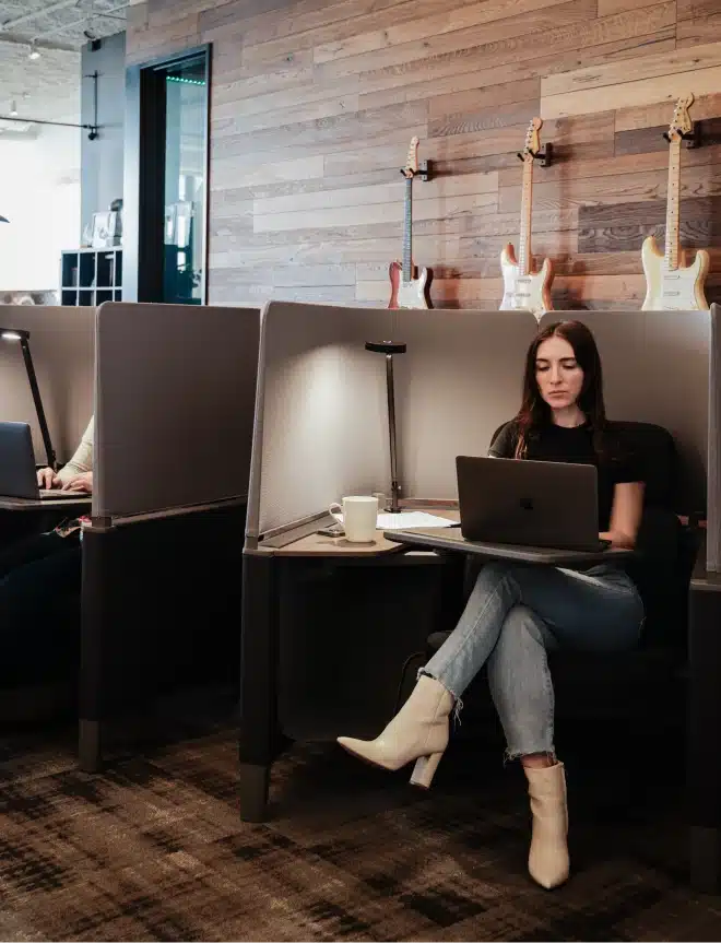 Creative professional seated in quiet nook with laptop and boots, working near wall-mounted guitars