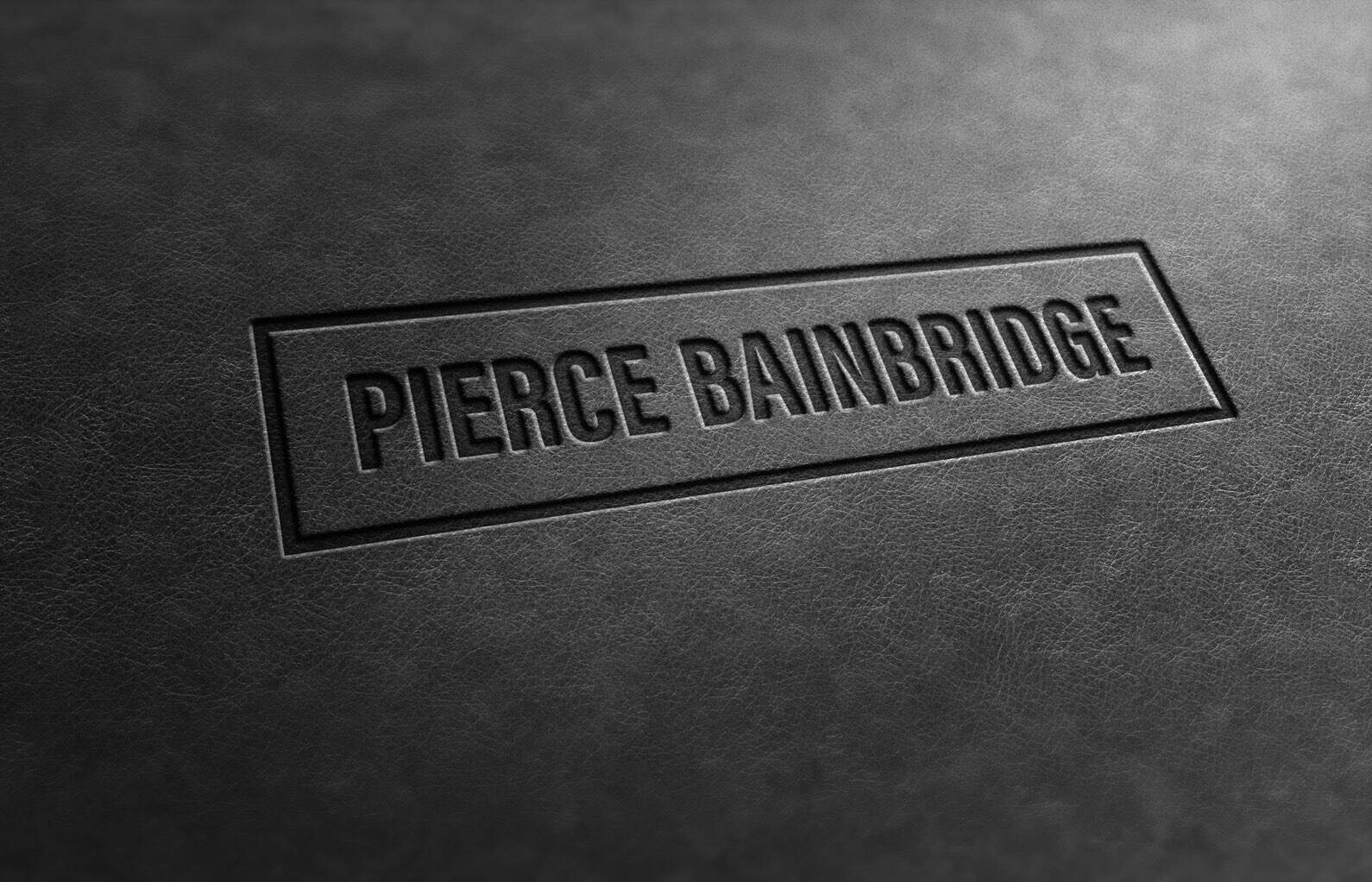 Embossed leather folder with Pierce Bainbridge branding centered on textured black surface