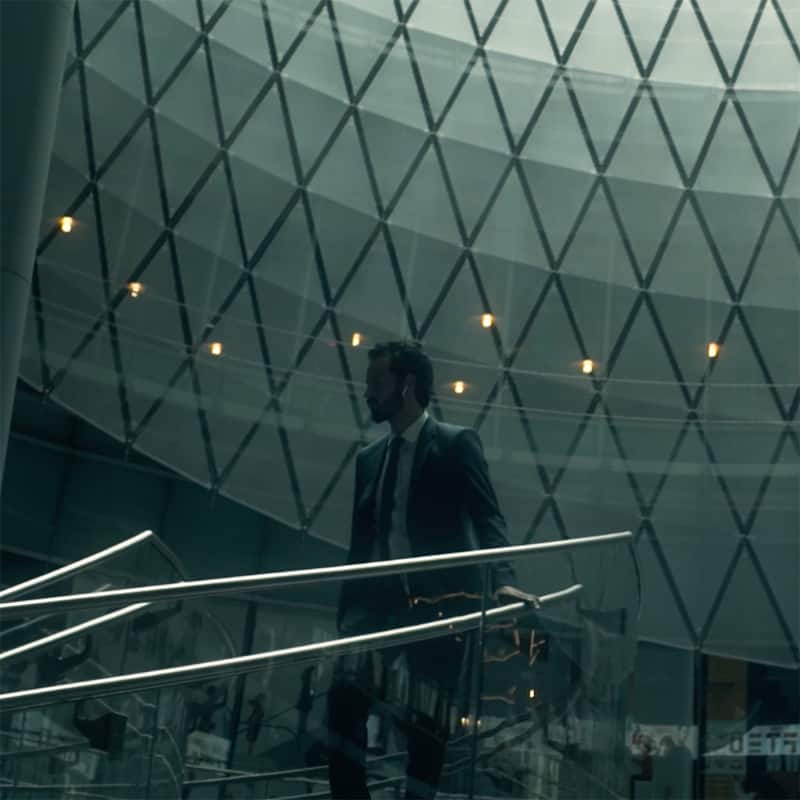 Businessman in suit descending modern staircase beneath geometric glass ceiling with moody lighting