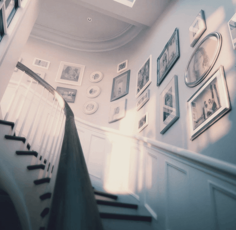 Curved staircase lit by skylight with family photo gallery displayed on soft blue wall