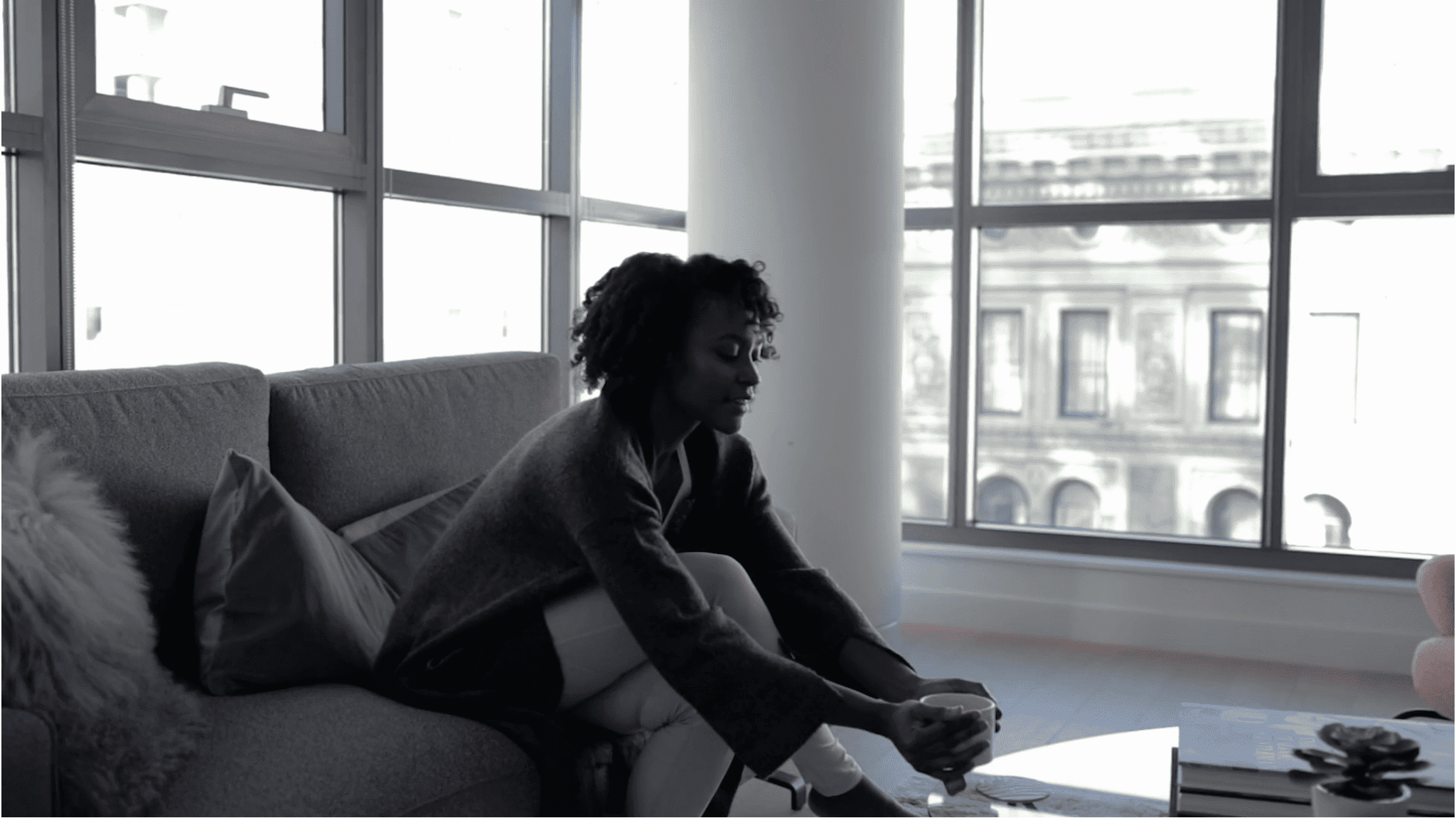 Woman relaxing on modern sofa in high-rise apartment with city views through large windows