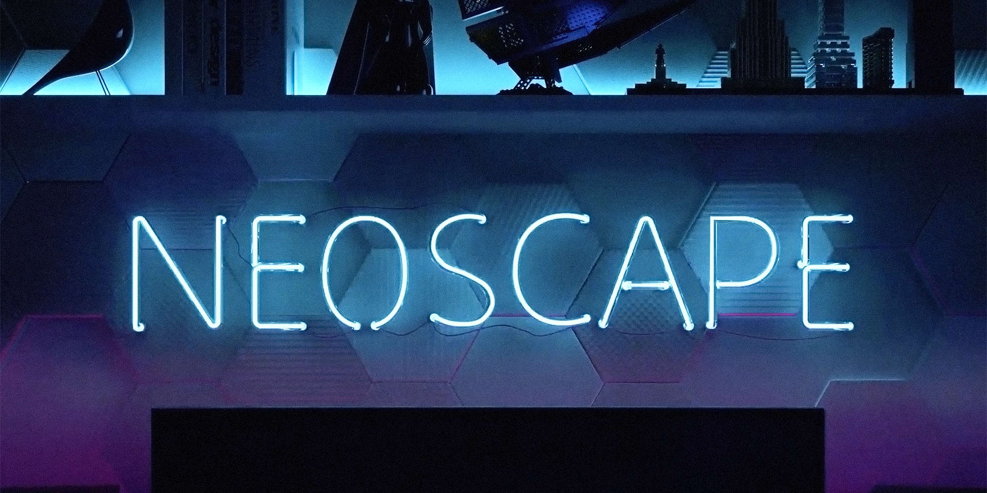 Blue neon Neoscape logo illuminated in front of hexagon wall art and architectural models