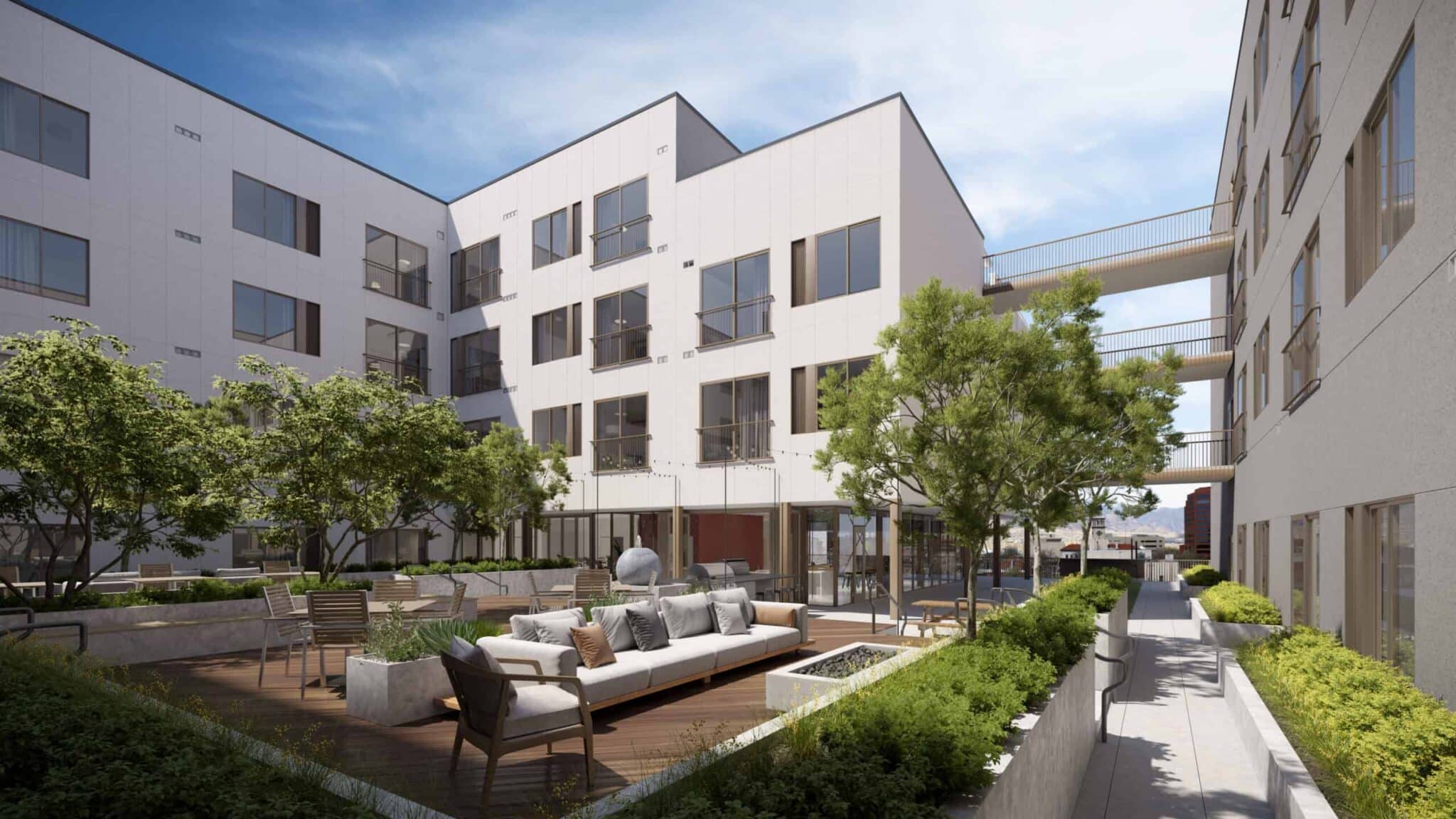 Modern courtyard with lounge seating, landscaping, and white apartment buildings under clear sky