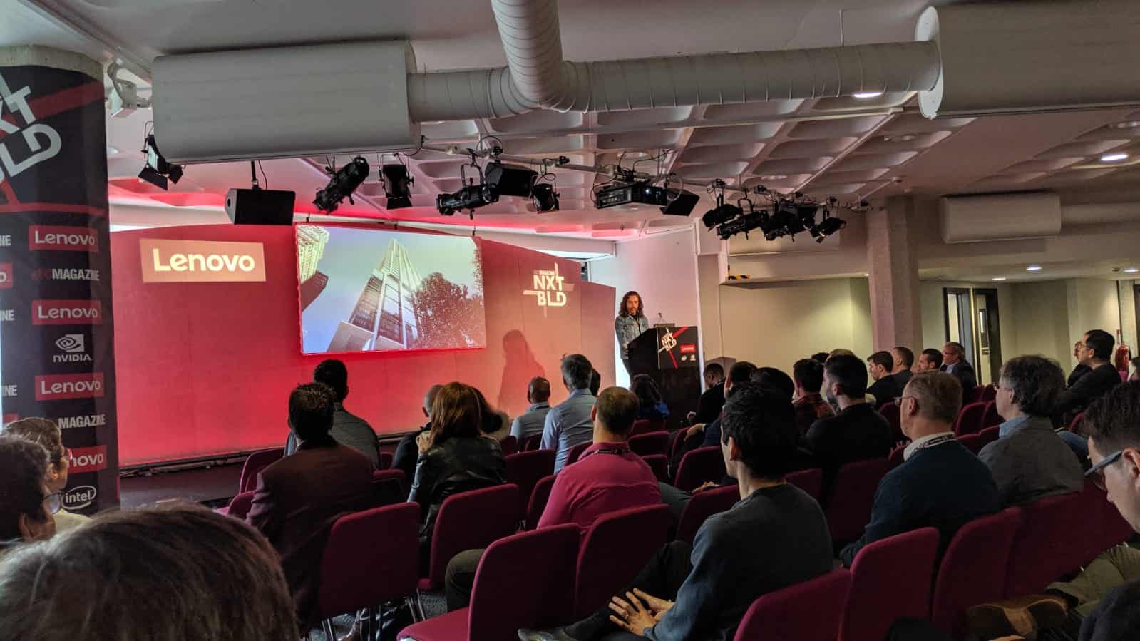 Presenter speaks at NXT BLD event in front of screen showing skyscraper image and Lenovo branding