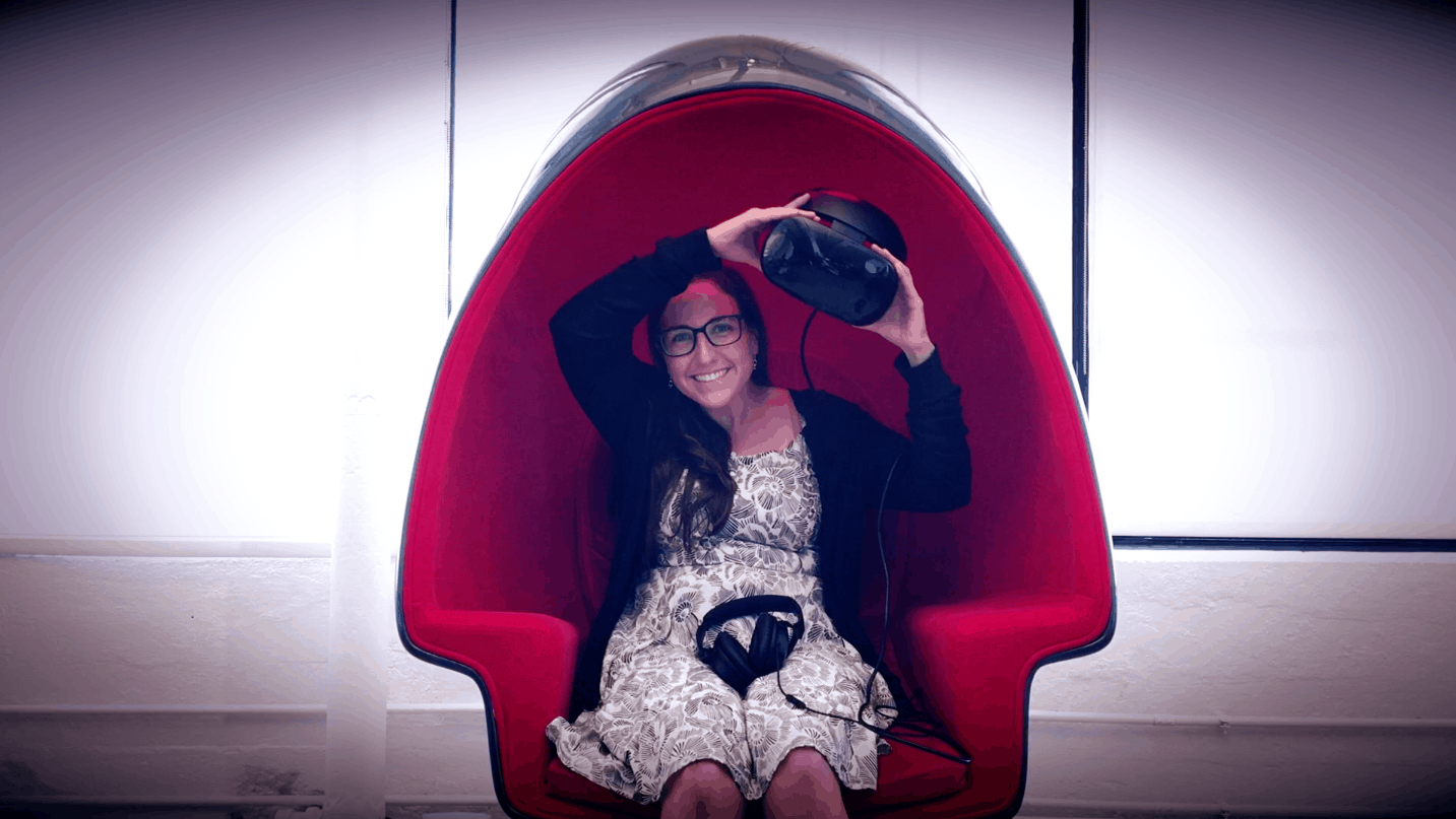 Smiling woman holds VR headset while sitting inside an egg-shaped Voyager pod chair