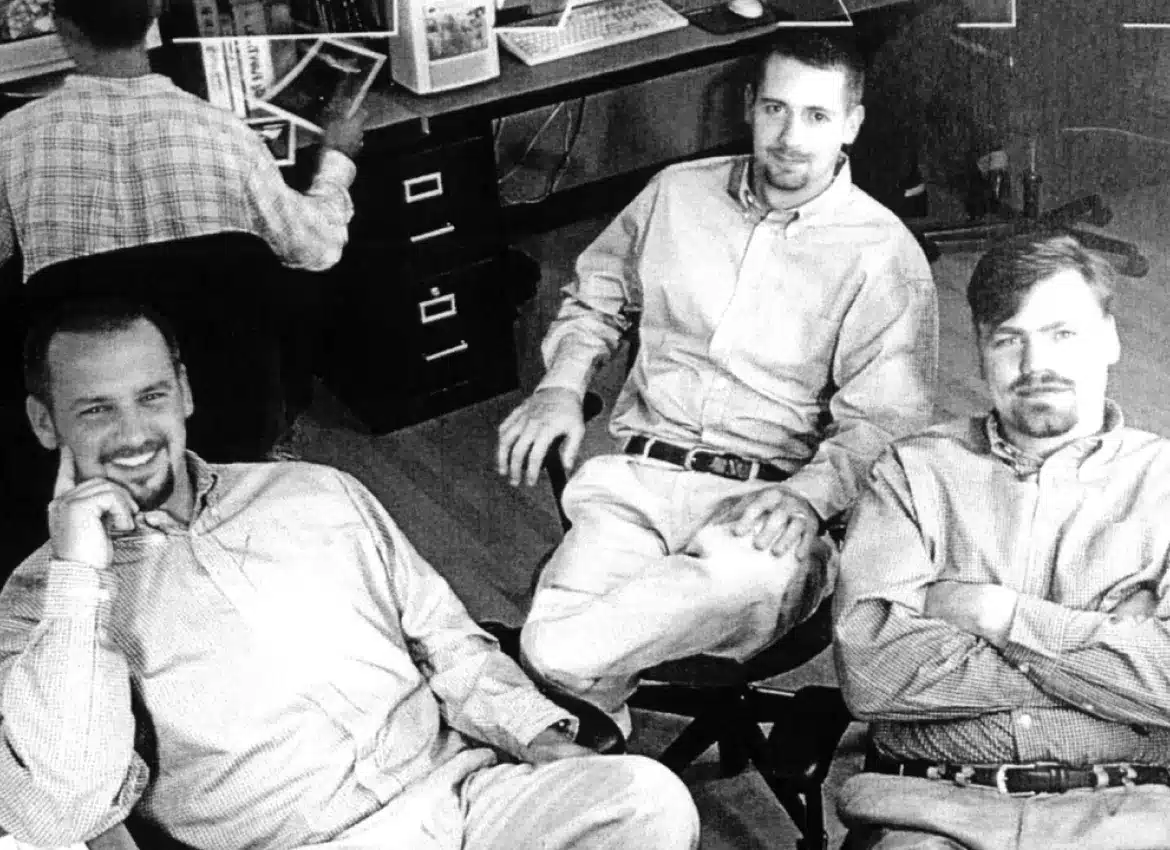 Vintage office setting with three coworkers in matching shirts, looking at the camera