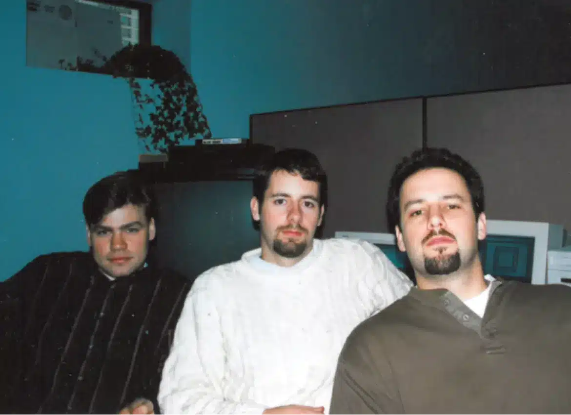 Vintage group photo from 1996 featuring three men in casual work attire relaxing indoors