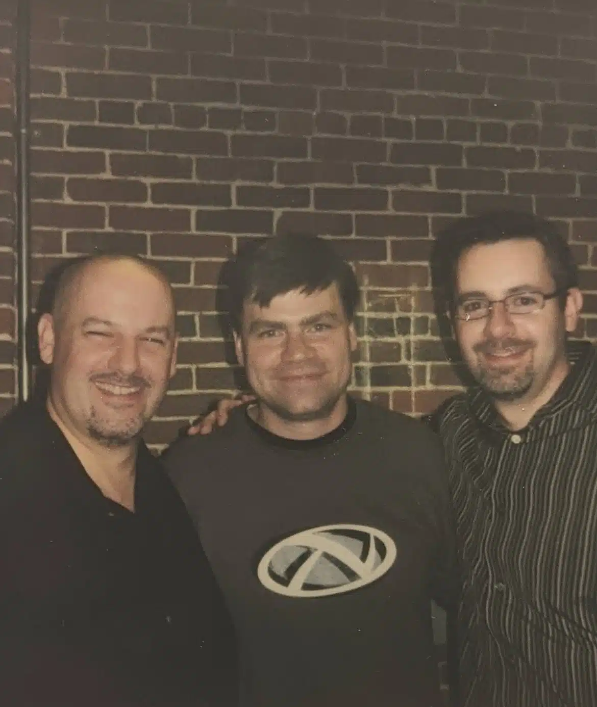 Casual photo of three partners close together in front of rustic exposed brick backdrop