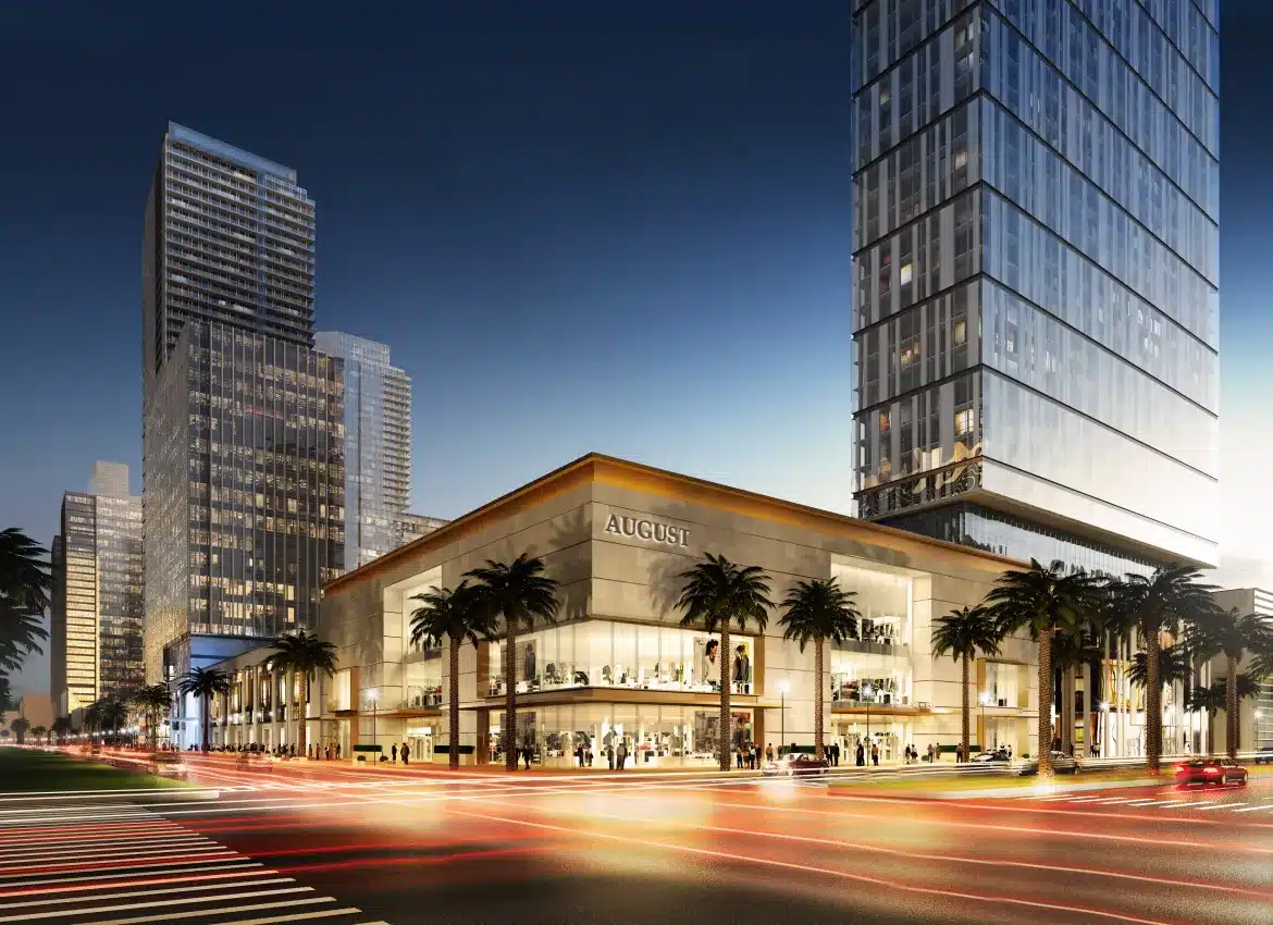 Modern luxury retail complex at night with illuminated storefronts and palm trees along urban streetscape