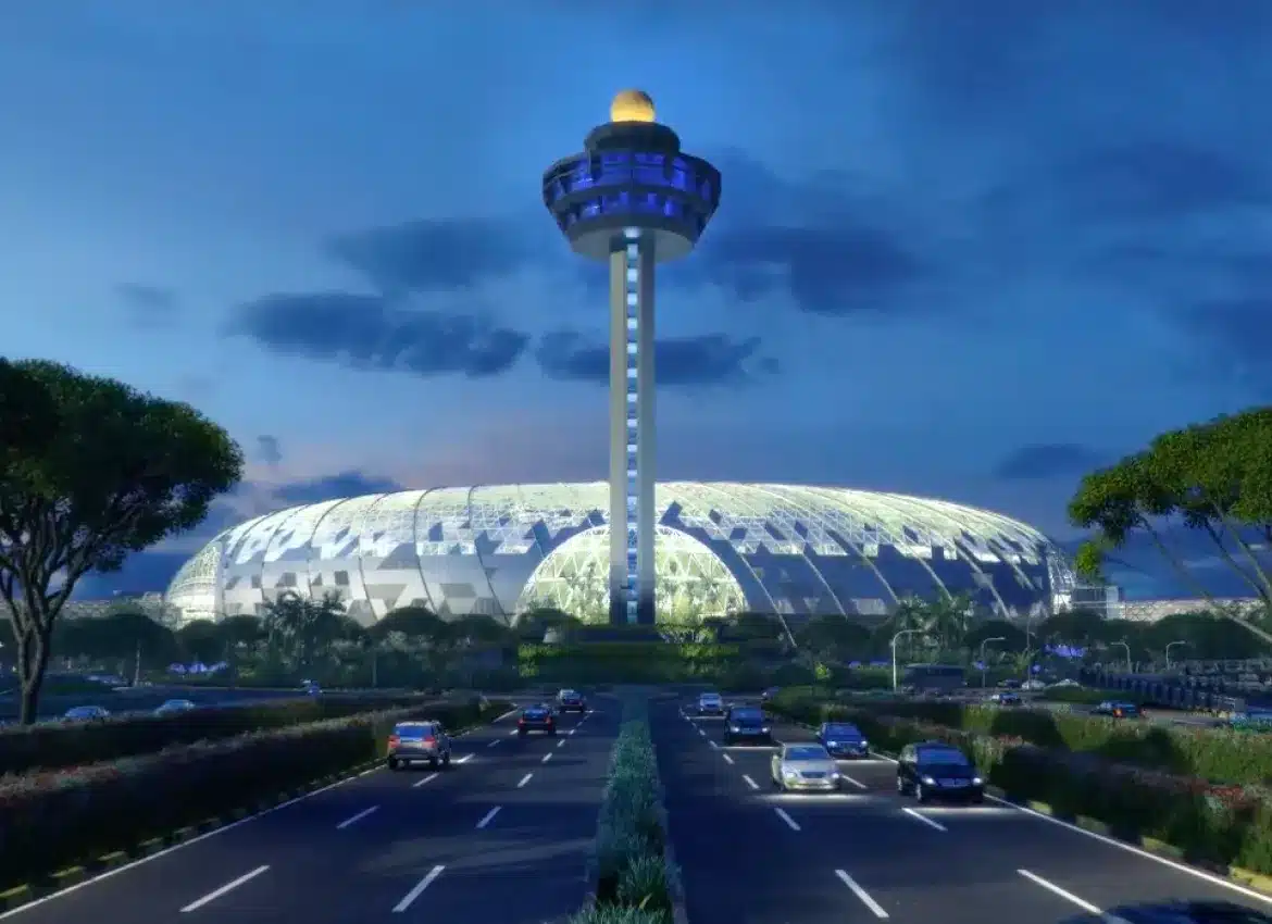 Contemporary illuminated sports venue with distinctive tall tower and surrounding road traffic