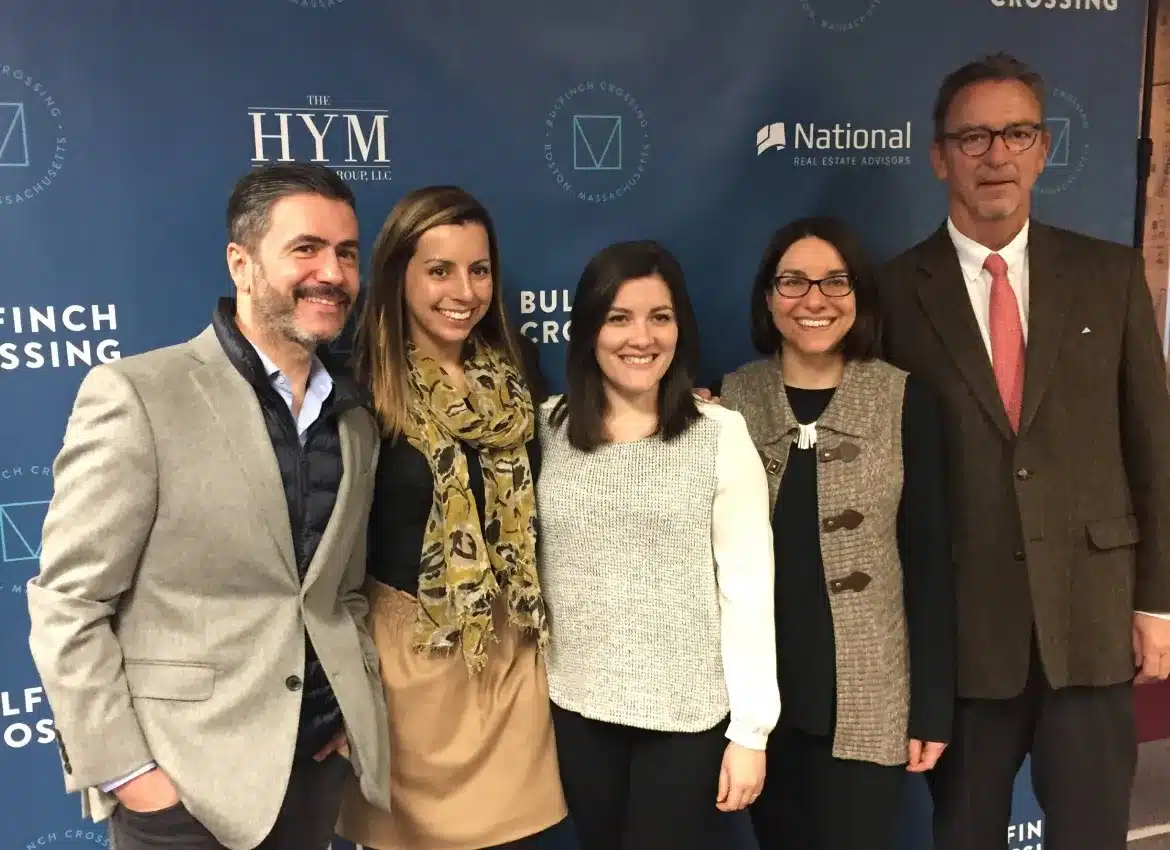 Group of professionals posing together at event with branded backdrop featuring sponsor logos