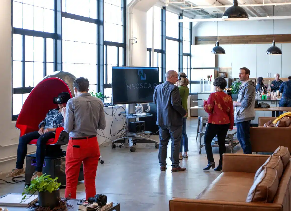 Office gathering with people networking around modern lounge featuring VR chair demonstration