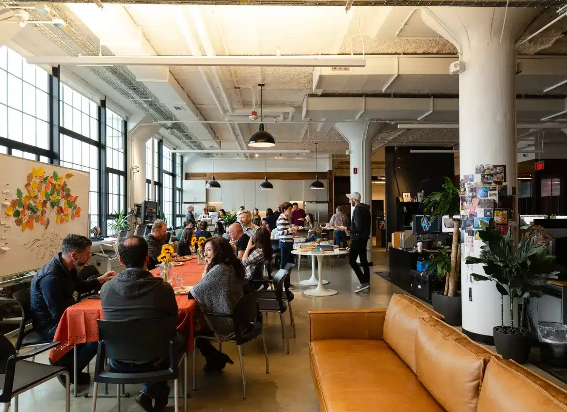 Office community gathering with people enjoying shared meal around decorated tables