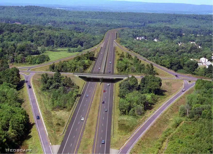 Aerial view of divided highway with cars passing under landscaped pedestrian bridge