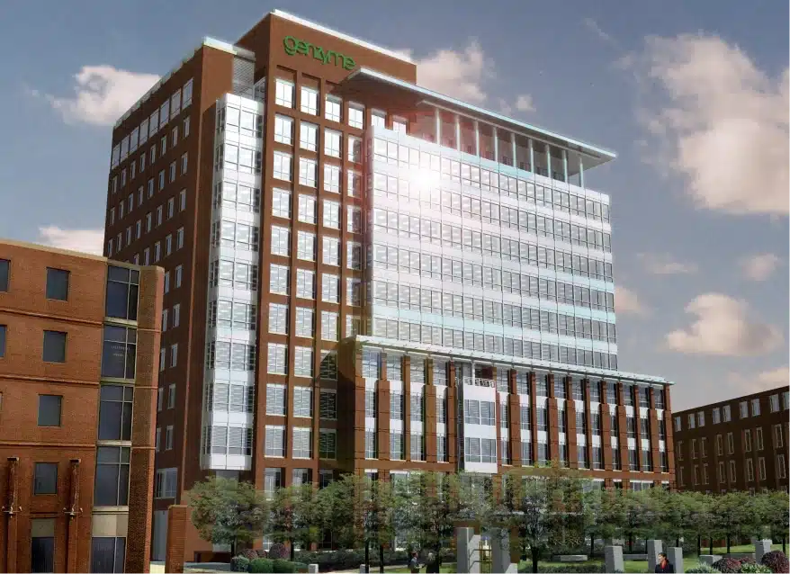 Modern glass office tower with brick base and logo near top reflecting morning sunlight