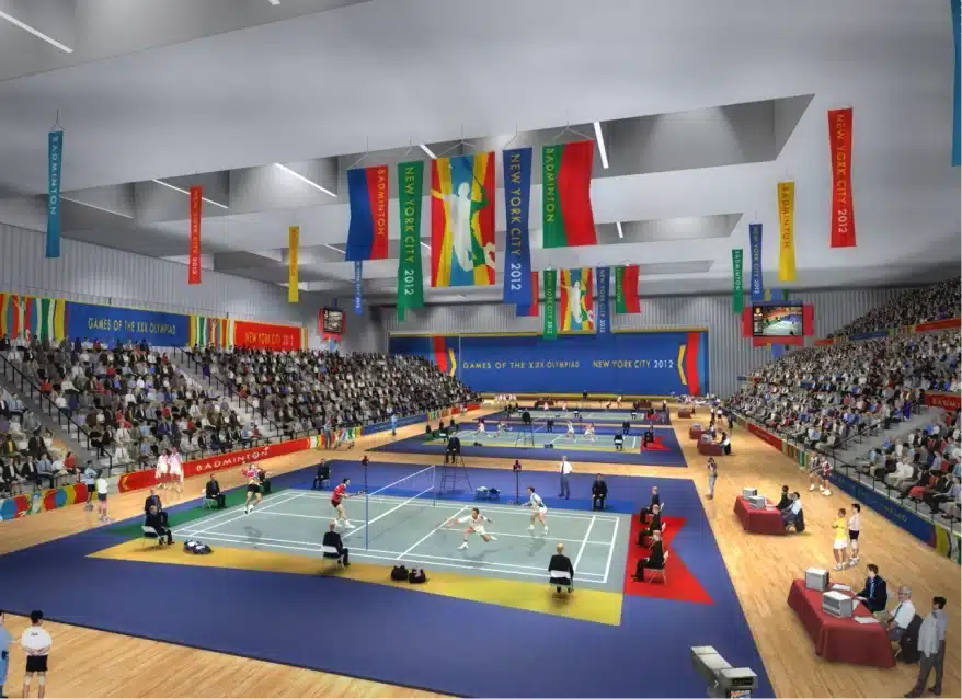Indoor badminton tournament with players competing on courts beneath colorful Olympic banners and crowded stands