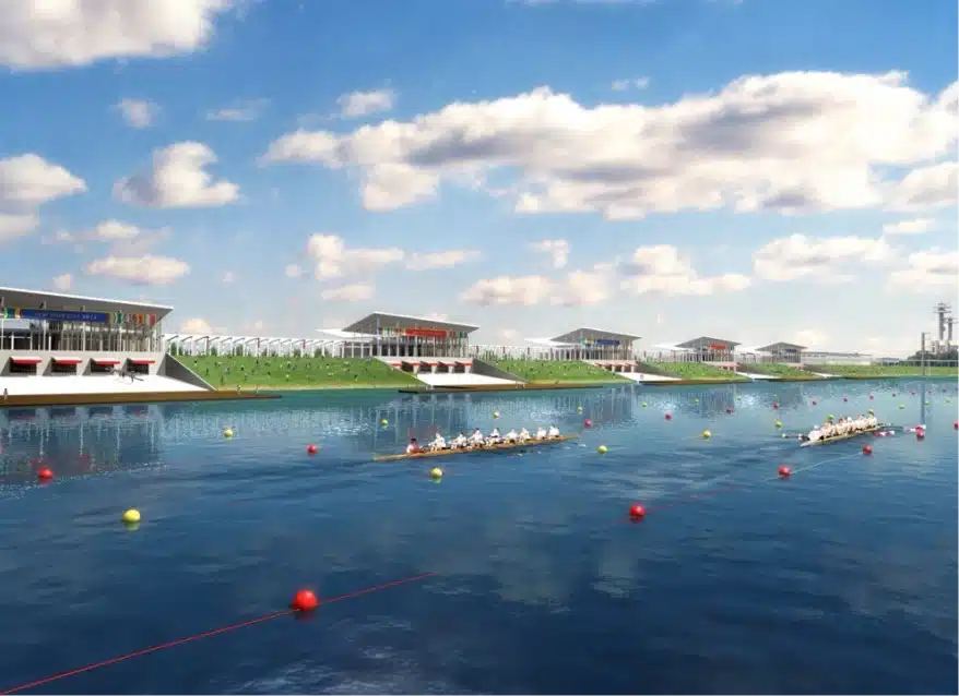 Rowers competing in long boats on Olympic watercourse with grandstands and modern facilities along shoreline
