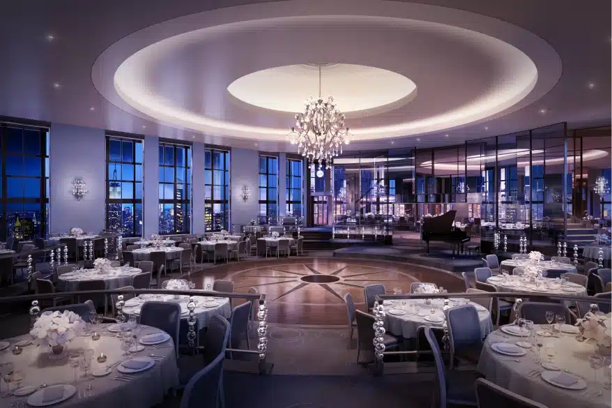 Elegant ballroom with chandelier lighting, round tables, and panoramic evening city skyline views