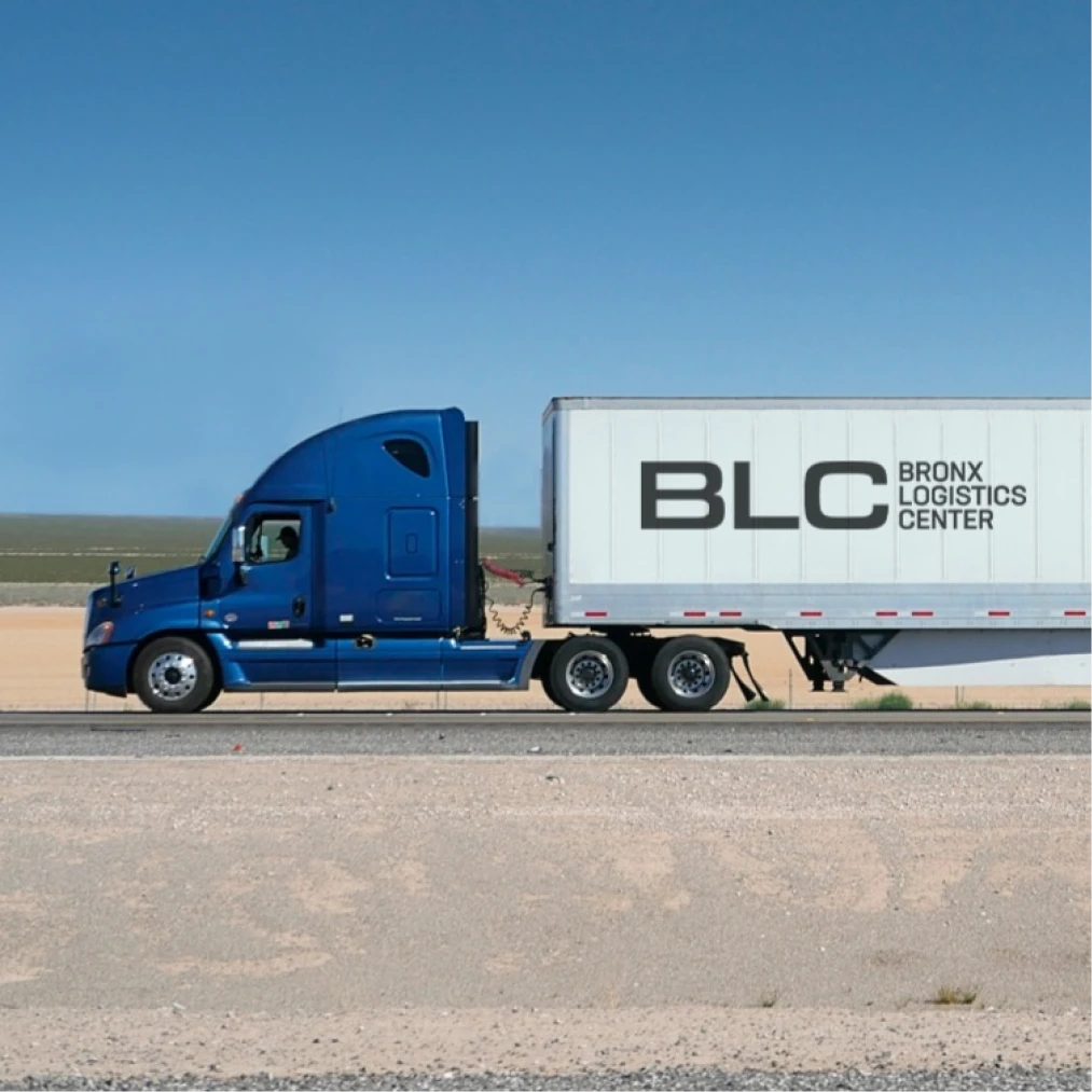 Commercial freight truck transporting Bronx Logistics Center trailer across rural roadway in daylight conditions