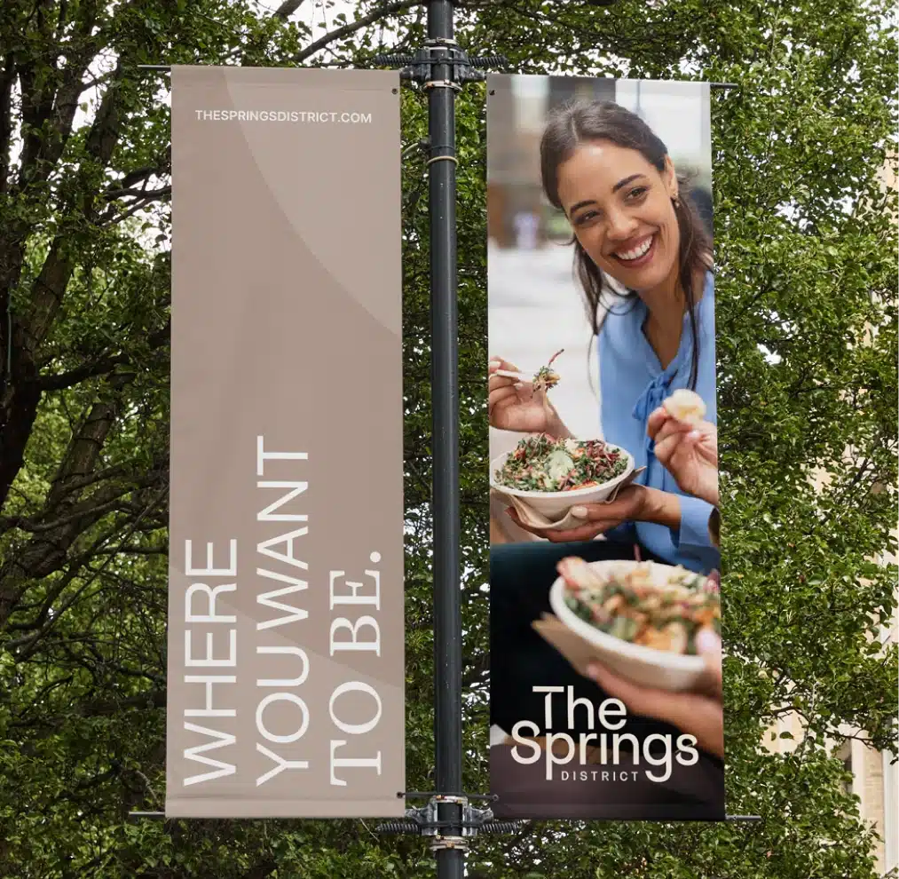 Street banners promoting The Springs District featuring lifestyle dining imagery and vibrant walkable neighborhood branding