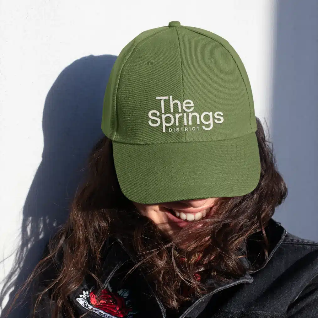 Branded green promotional hat displaying The Springs District logo with modern lifestyle styling