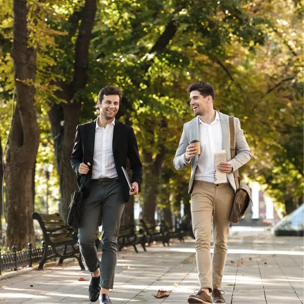 Young professionals enjoying conversation while walking outdoors with takeaway coffee in landscaped city park setting